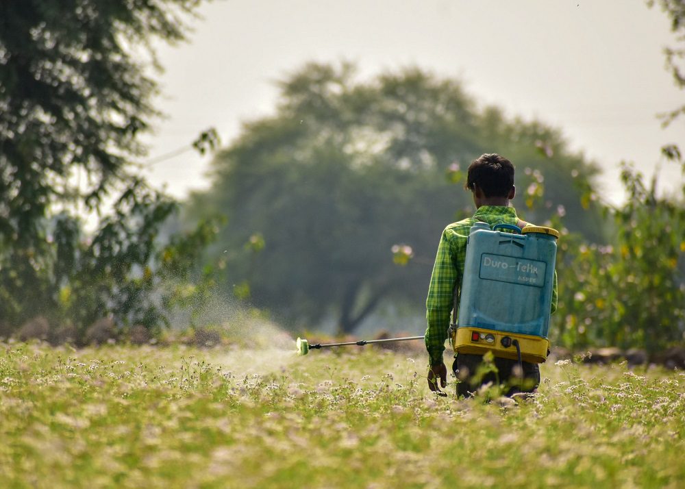 Worker spraying field representing exposure assessment
